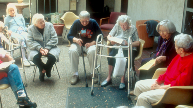 Elderly people sit in a circle in a care facility.