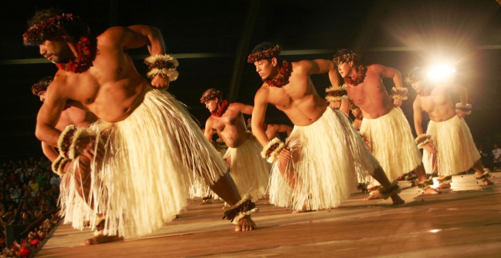 Men in grass skirts perform a traditional hula dance.