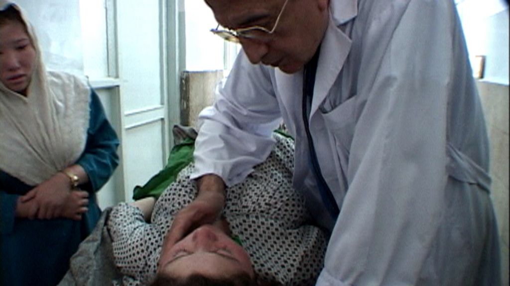 A man in a white doctor's coat places his hand against the cheek a woman lying on a table