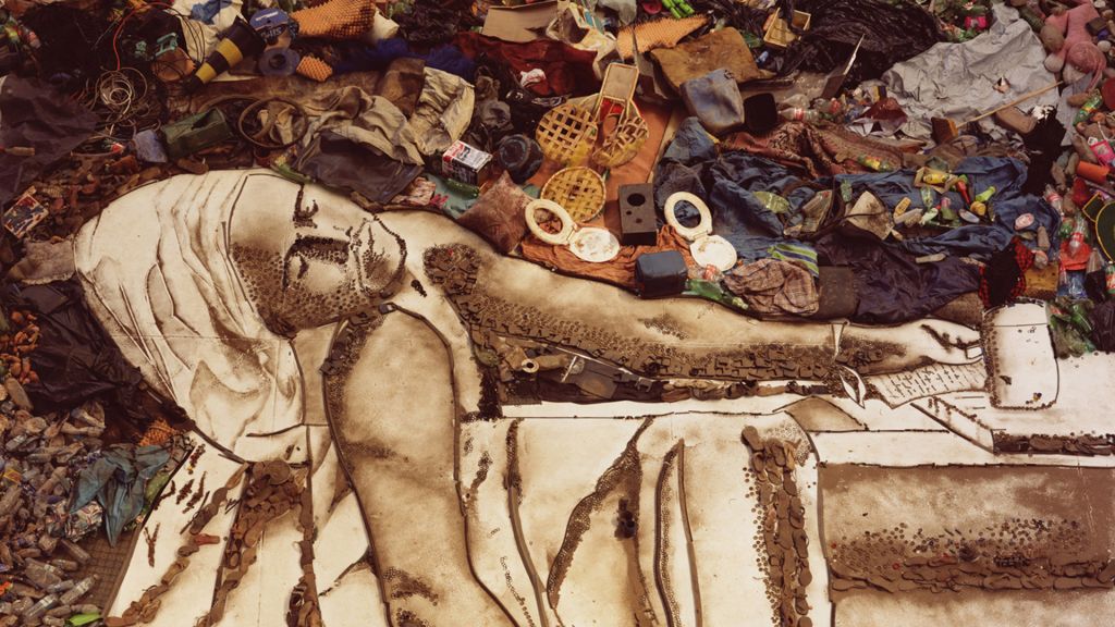 Vik Muniz portrait of man in a bathtub with shawl on his head with garbage dump in background, recreating Jacques-Louis David's famous painting, "The Death of Marat."