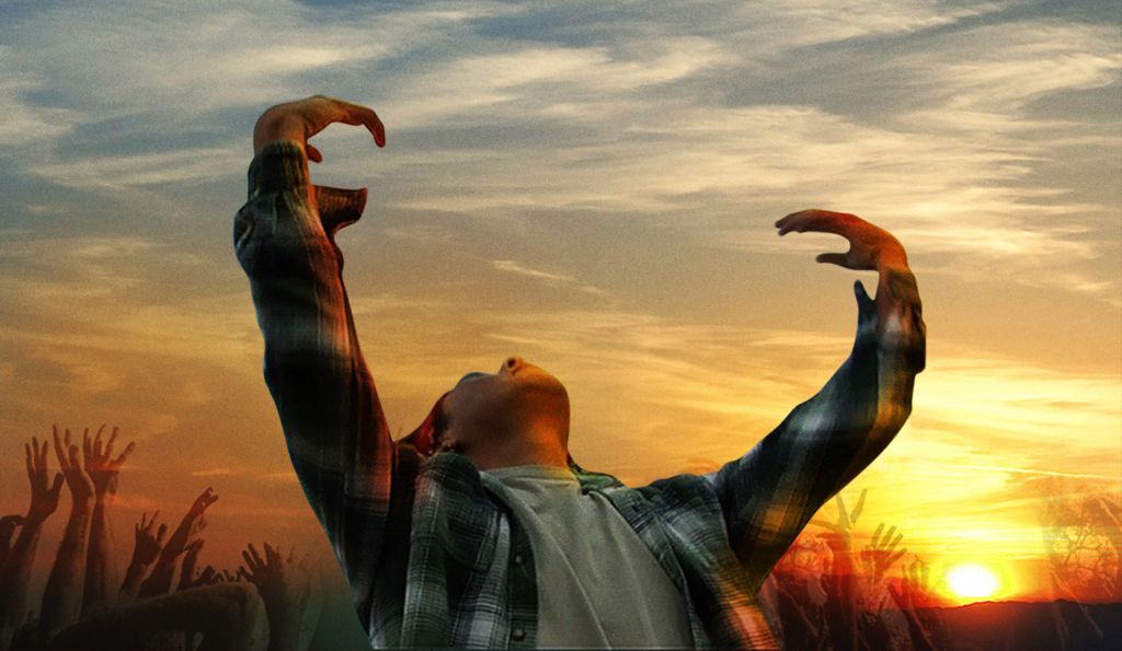 Young boy raises his arms against a golden sunset.