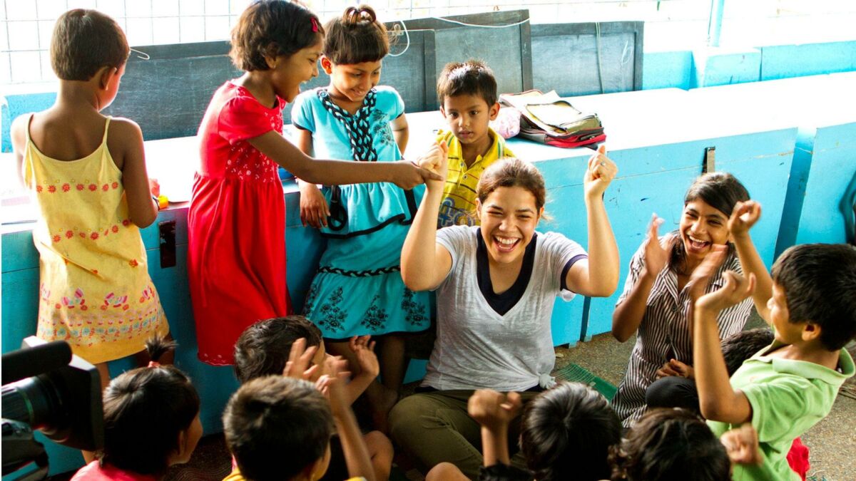 Actress America Ferrera surrounded by a group of Indian children, all cheering and having fun.