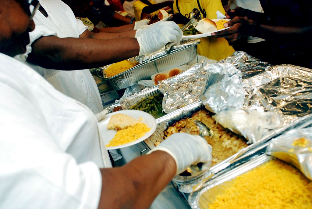 African American chefs serve plates of soul food from aluminum containers.