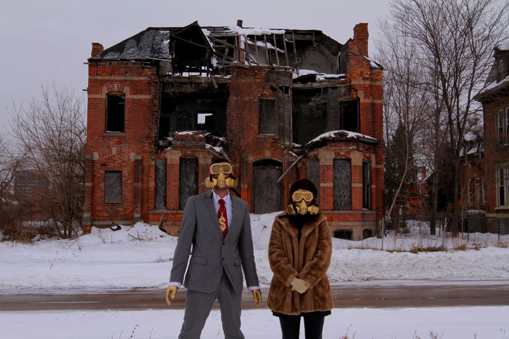 A man and woman wearing gas masks stand outside a derelict home on a snowy street in Detroit.