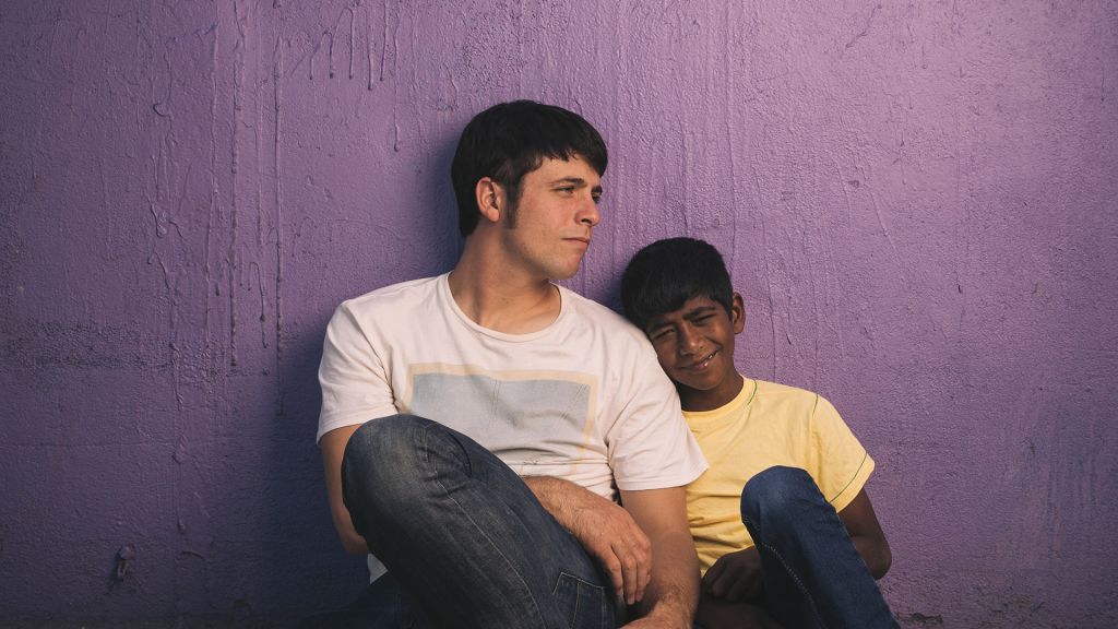 Rocky Braat sits against a purple wall with young Indian boy.