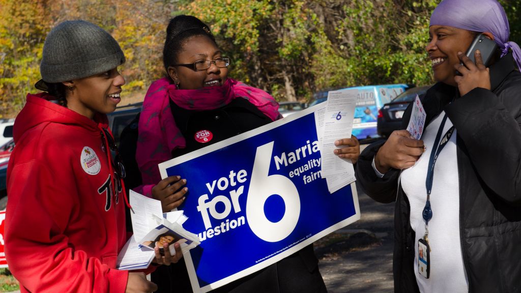 African American protestors carry a sign that reads "Vote for Prop 6."