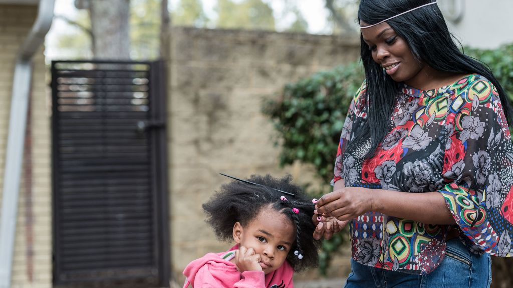 An African American mother works on her daughter's hair.