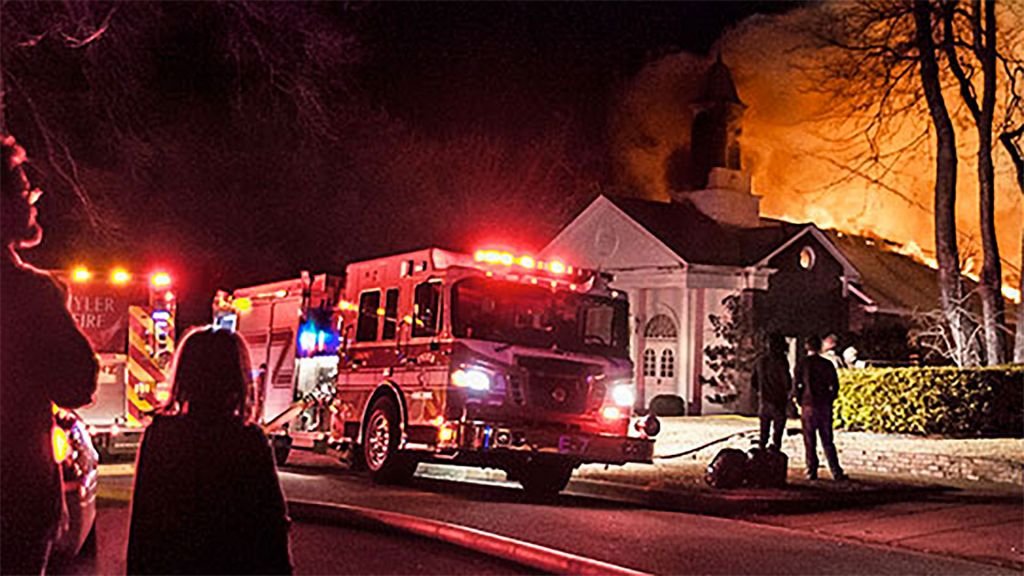 Emergency response vehicle with flashing lights parked outside burning East Texas church.