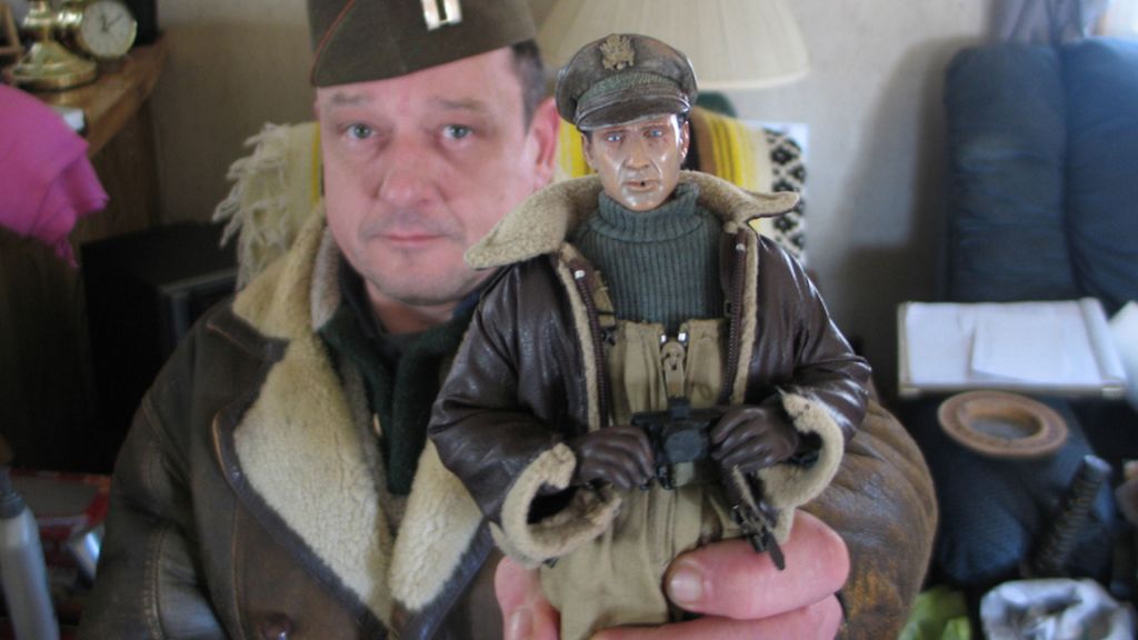 artist Mark Hogencamp holding up a doll character for his fictional town Marwencol