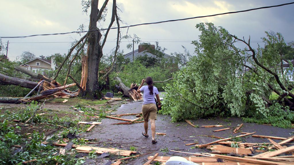 Woman walks through downed trees and debris after a tornado.