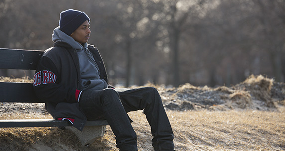 Young African American man sits on a park bench in winter clothing.