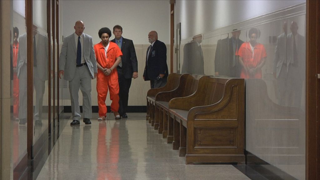 An inmate is led by lawyers and law enforcement through courthouse hallway.