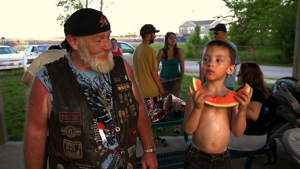 Biker Ronnie "Stray Dog" Hall watches a kid eat a watermelon.