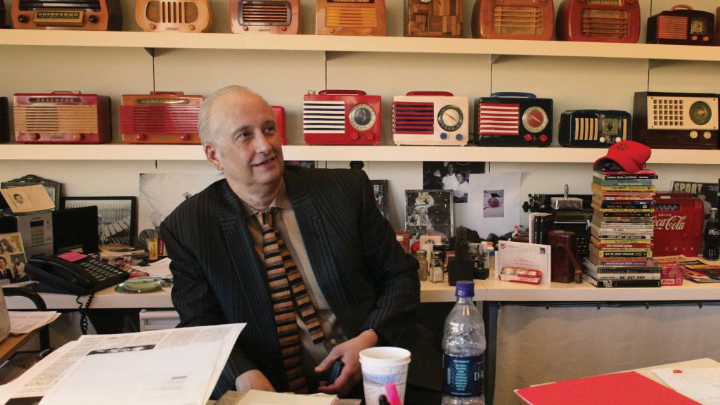 Man sits in office surrounded by vintage transistor radios.