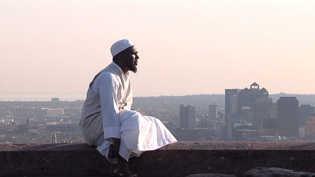 An imam gazes at the city from a rooftop vantage.