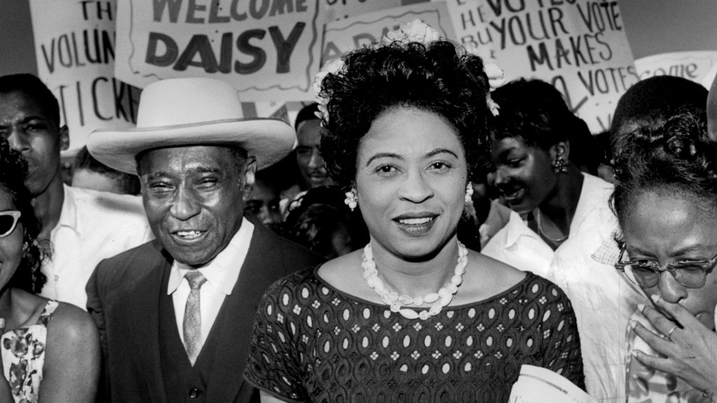 Daisy Bates marches with a crowd of supporters carrying signs of support.