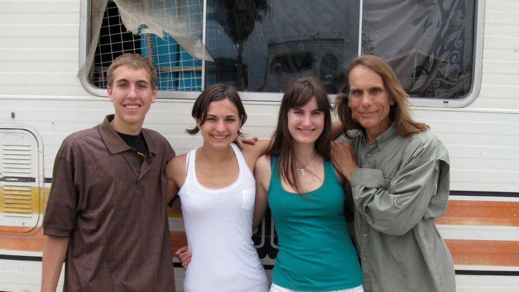 Four siblings stand in front of a motor home smiling for the camera.