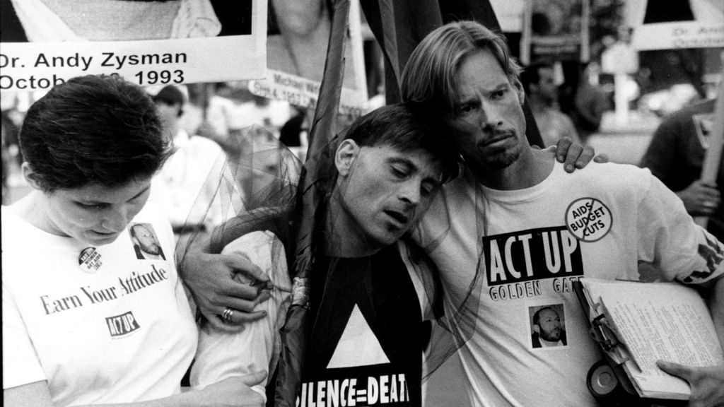 Archival photo of ACT UP AIDS activists embracing during a protest.