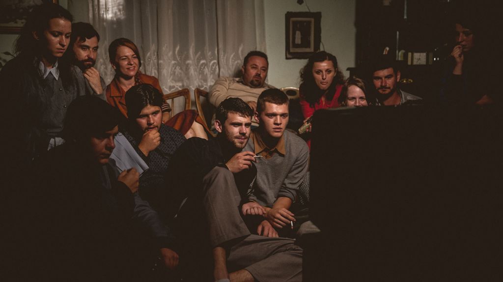 A group of people are crowded around a television set captivated by a film.