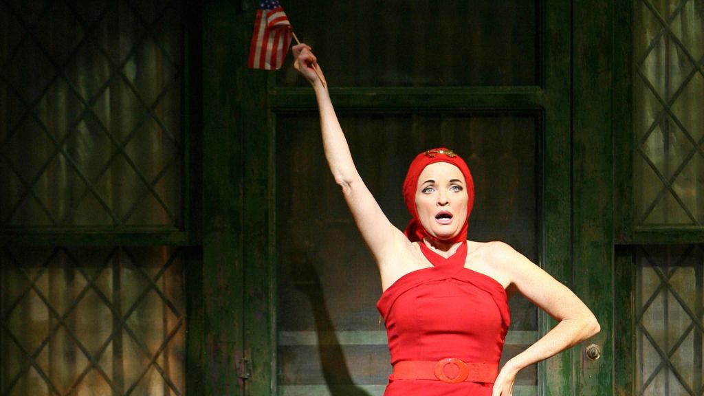 A woman on stage wearing a red dress and head scarf