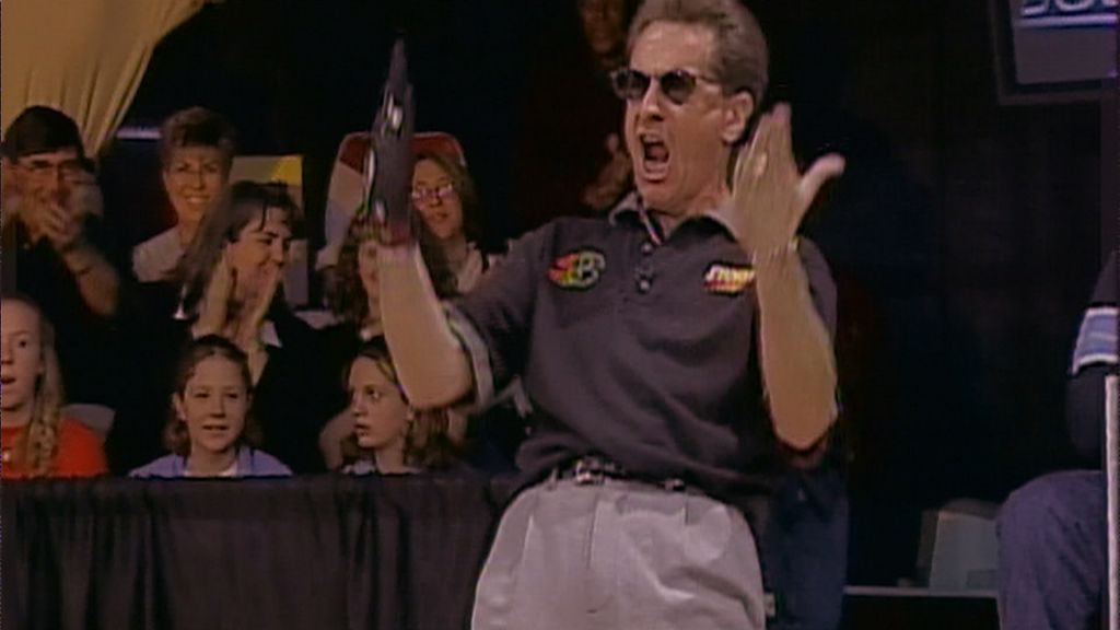 A bowler wearing sunglasses throws his arms up in excitement