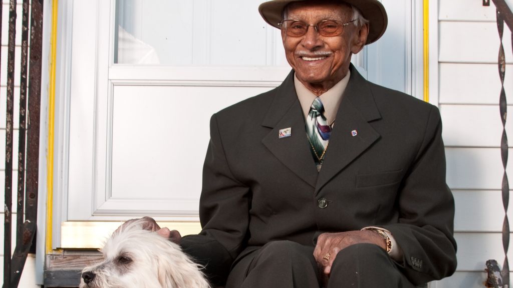 A smiling man in a suit sitting on a front stoop next to a small dog