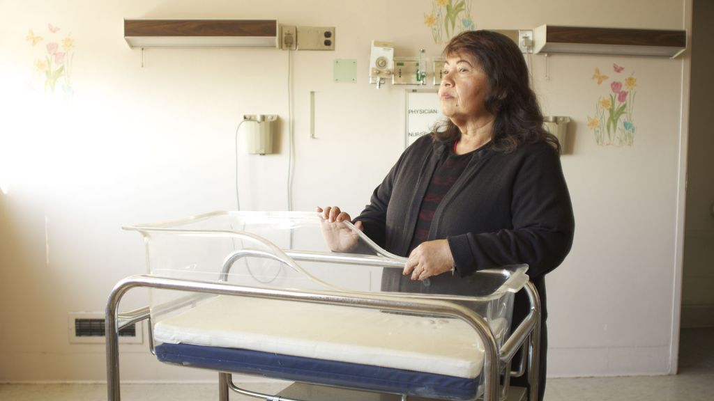 A mother stands before an empty incubator.