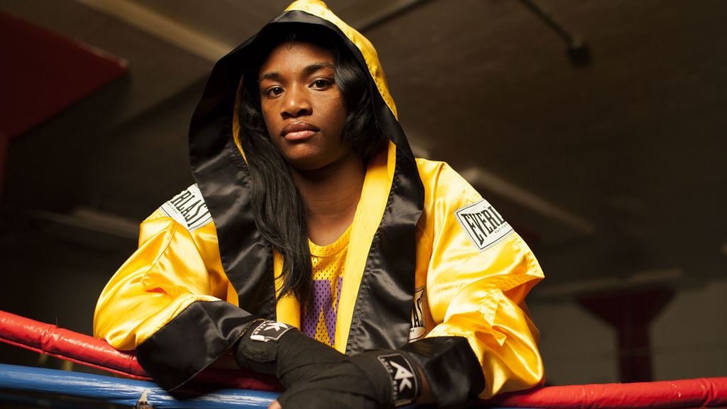 Claressa "T-Rex" Shields stands in the boxing ring in a gold robe.