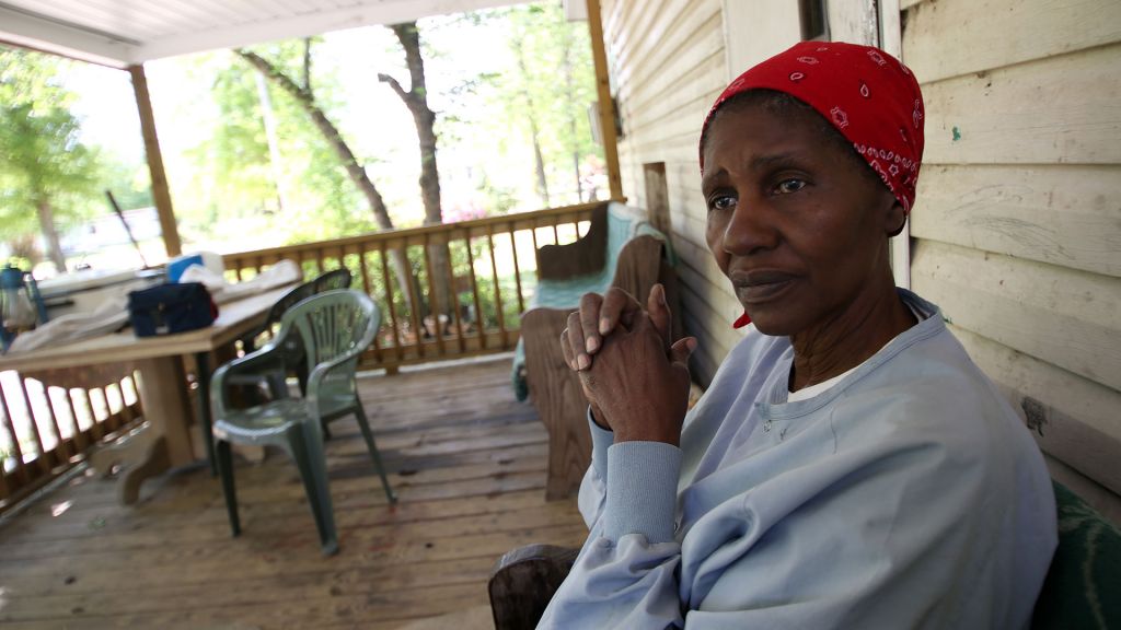 An elderly woman sits on her porch.