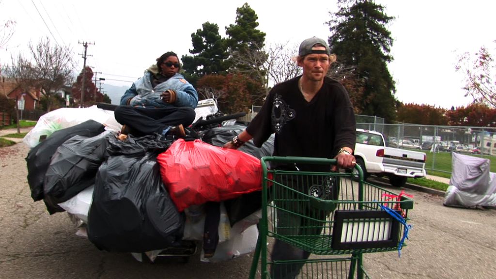 A man and a woman transport a grocery cart heaped with bags full of recycling they collected in Oakland, CA