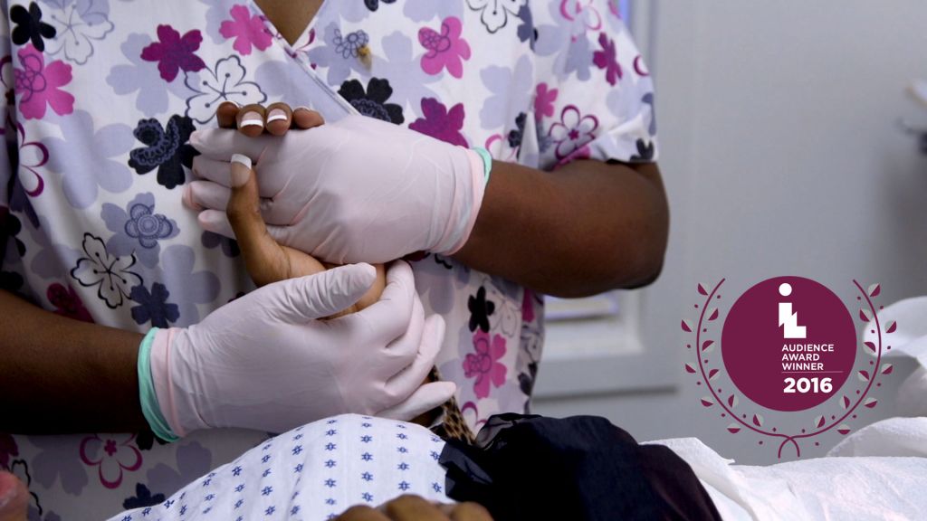 A nurse wearing latex gloves clasps the hands of a woman receiving an abortion (includes IL Audience Award graphic)