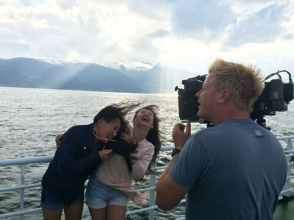 Alex and Mia laugh while a film cameraman shoots them on a boat in Norway