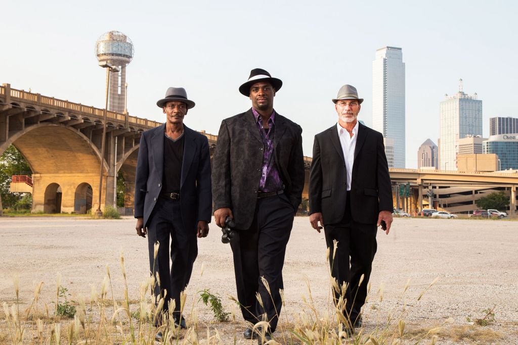 the three men of True Conviction pose in suits and hats on an industrial site