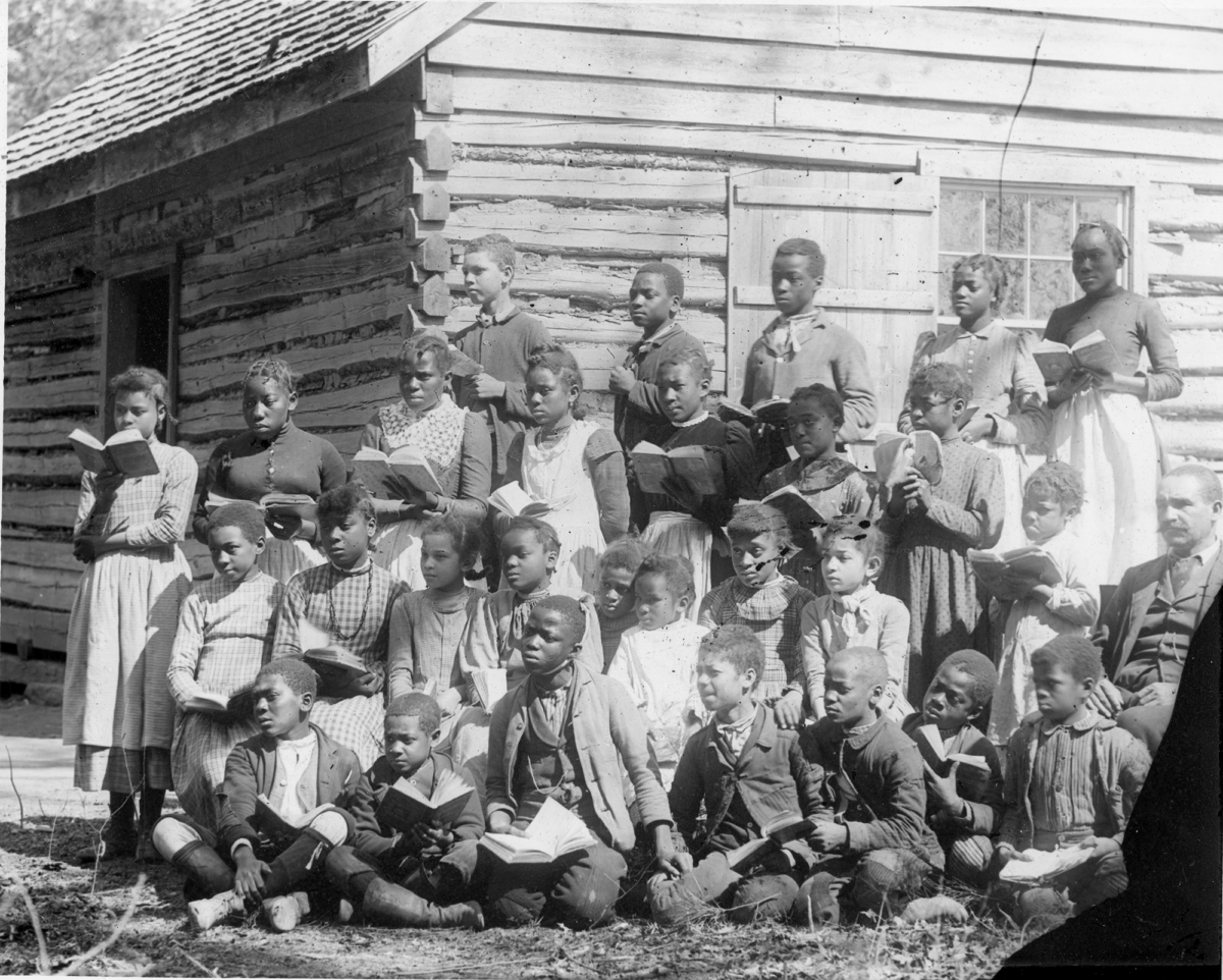 Group of children outside of school with books in hand looks colonial