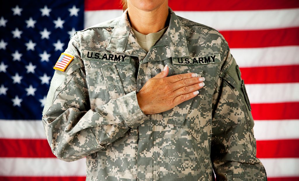 Woman soldier in the army pledging allegiance with US flag behind her; image by By Sean Locke Photography and Shutterstock