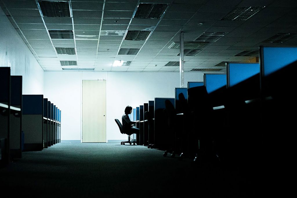 Dark room full of cubicles with one "cleaner" working late