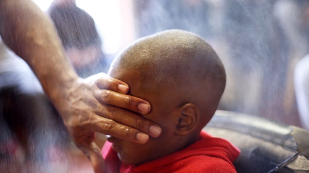 a child gets a haircut with hair powder, shielding his eyes, in Hale County