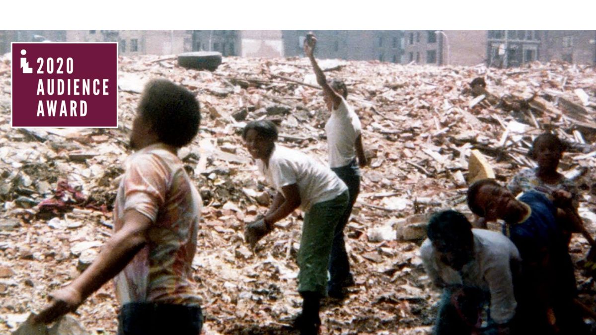 A group of people with dark skin tone help to clean up a large pile of rubble. The 2020 Audience Award logo is in the corner.