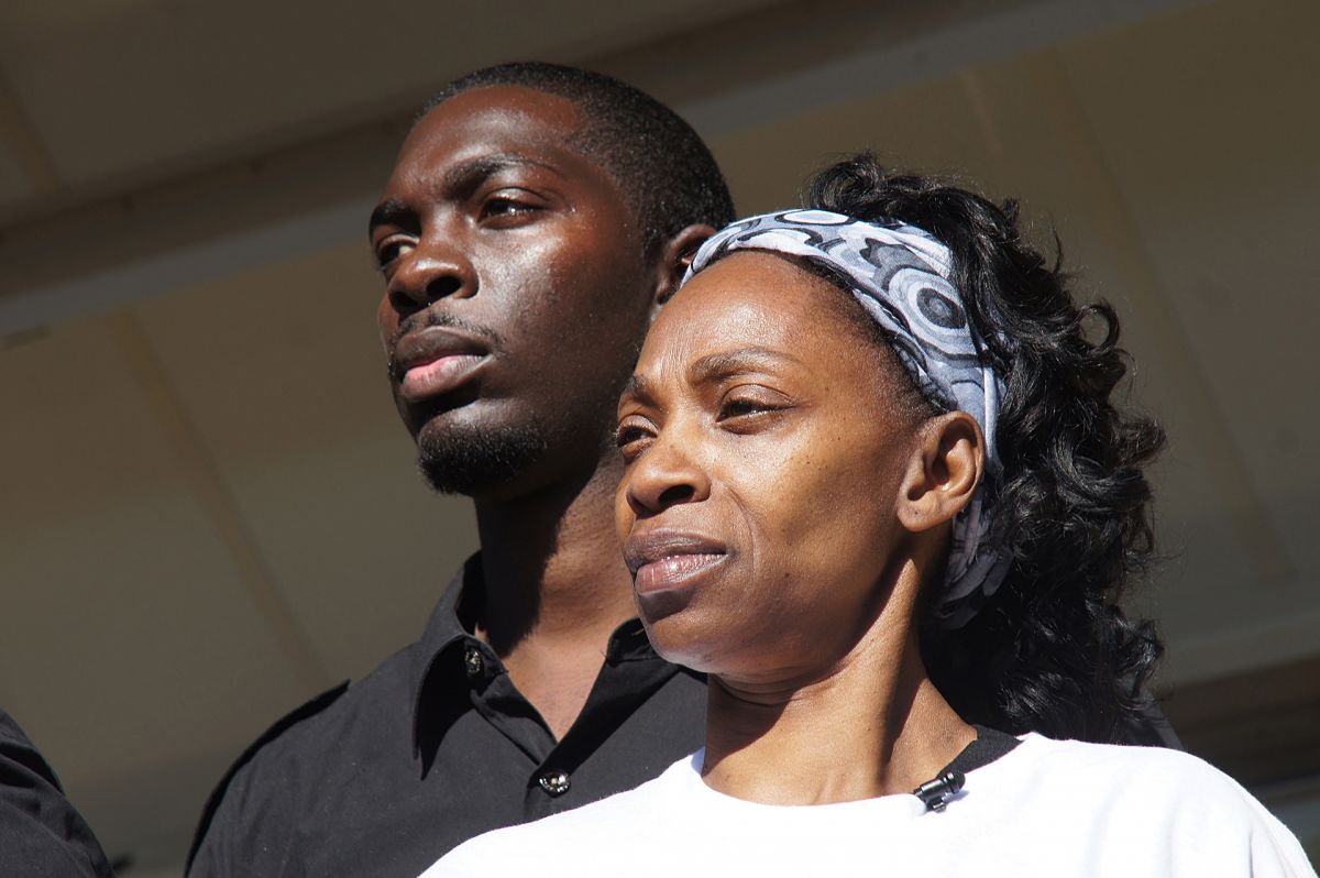 A man and a woman, both with dark skin tone, stand together and look off camera.