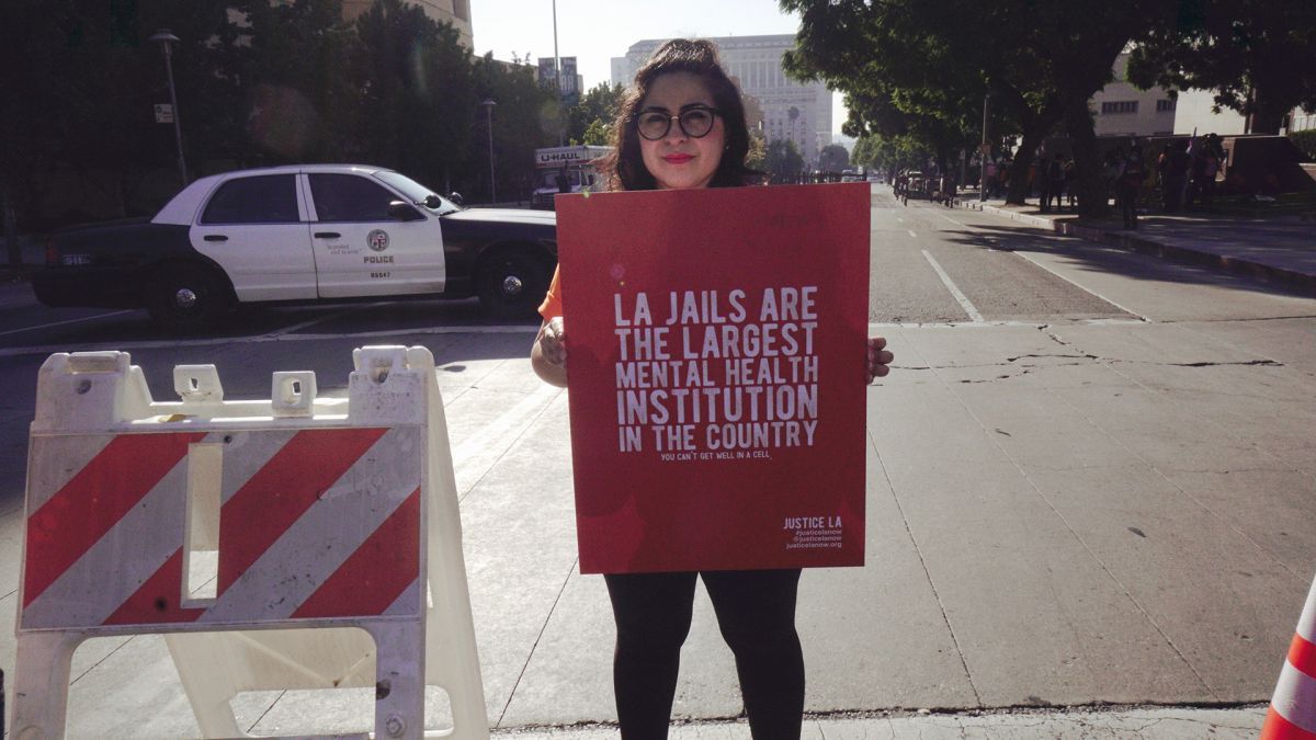 woman holding a red sign that reads La Jails are the largest mental health institution in the country you can't get well in a cell