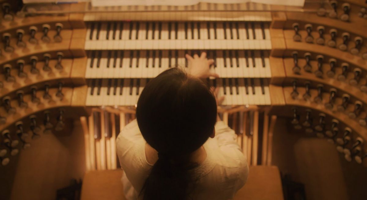 An overhead shot of a woman playing two of a pipe organ's three keyboards.