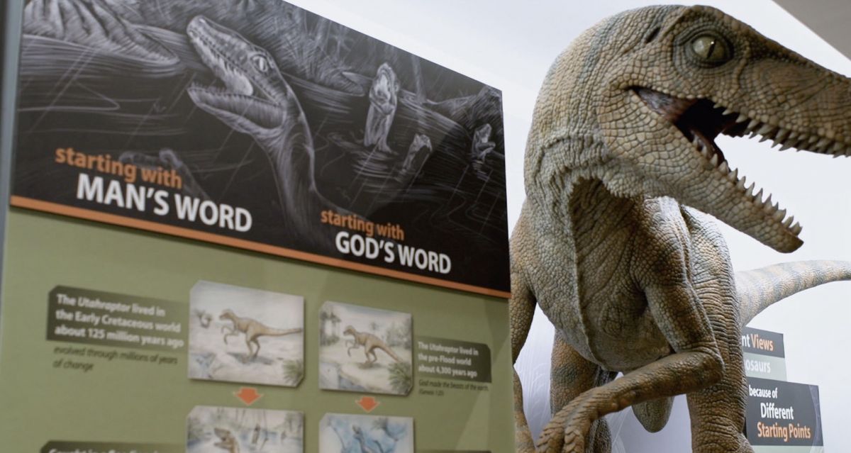 A large animatronic dinosaur stands next to a Christian creationist sign about "God's Word" at a creationist museum.