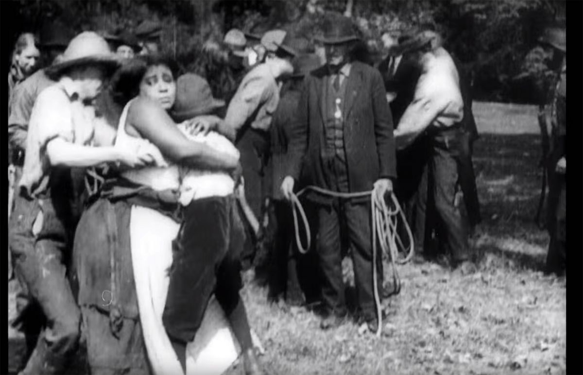 Still from the 1920 film "Within Our Gates" showing a mob of white men preparing to lynch a young Black boy, while a woman hugs him.