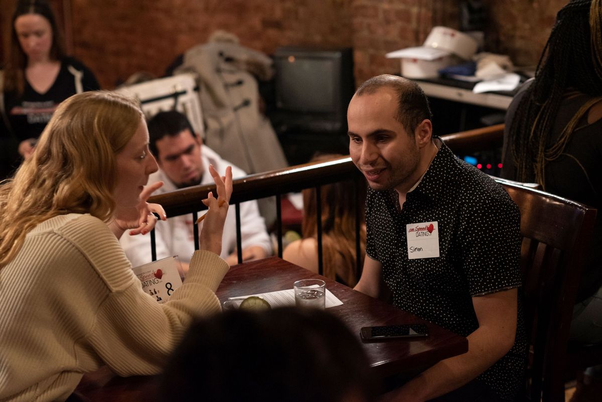 A blind man with light skin tone on a date at a speed dating event with a blond woman with light skin tone.