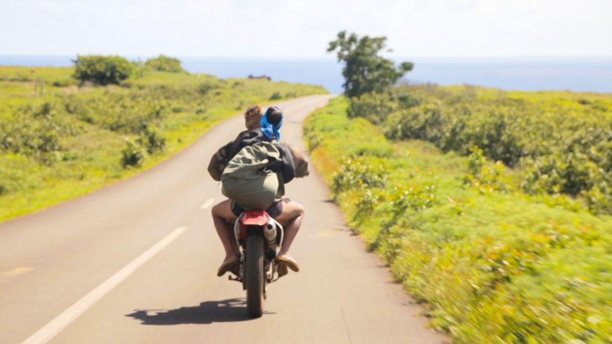 Two people riding a motorbike on an empty road by the seaside on Rapa Nui.