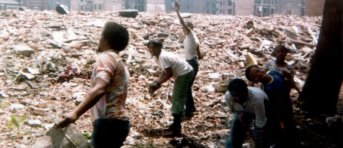 A group of people with dark skin tone help to clean up a large pile of rubble.