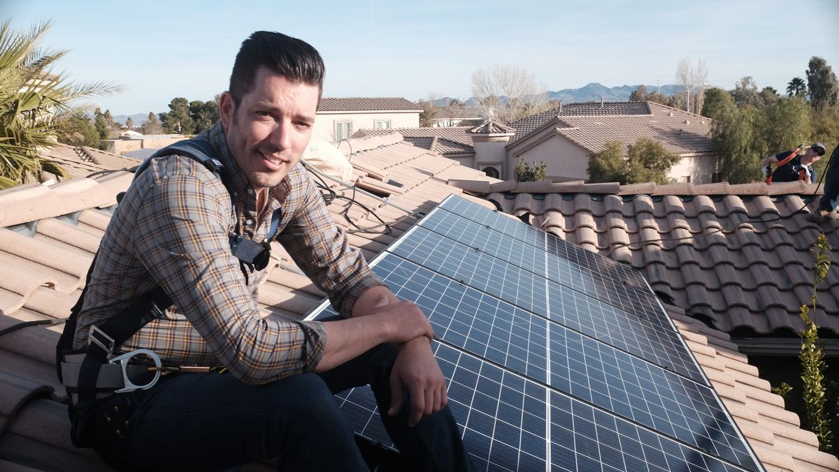 Jonathan Scott sits on a Spanish tiled roof that's covered in solar panels.