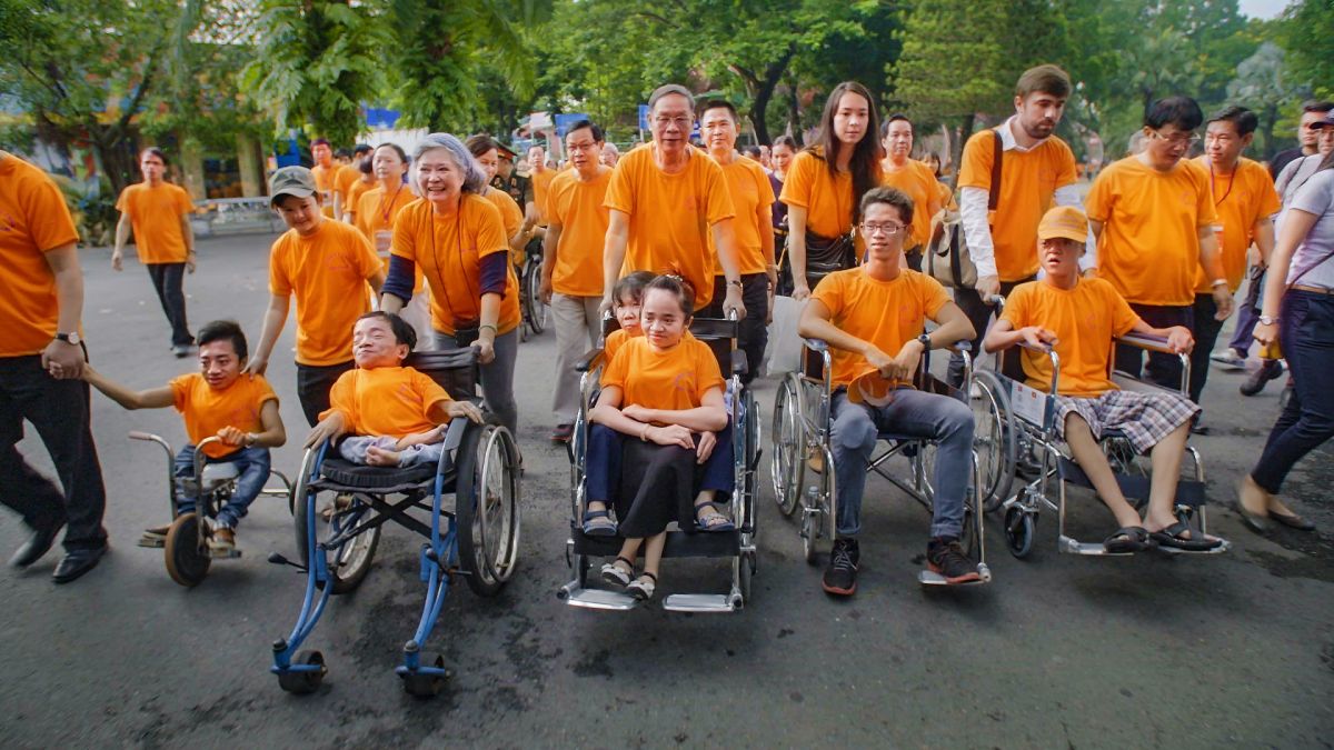 A large group of people in orange shirts march together. In the front of the line is a group of people using wheelchairs and other assistive devices.