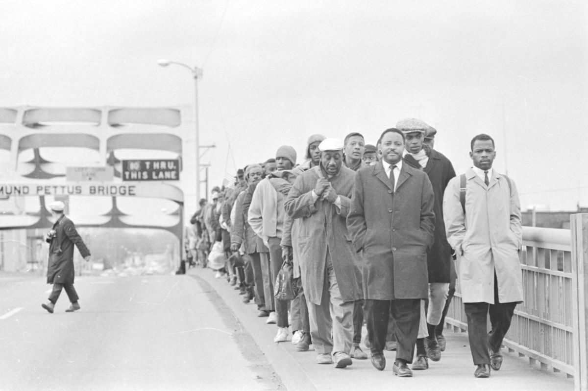 Black and white photo from 1965 showing John Lewis and many other civil rights protestors walking over the Edmund Pettus Bridge in Selma, Alabama.