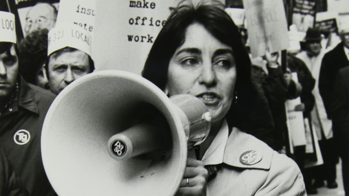 Black and white photograph of a woman speaking into a megaphone at a rally for equal pay.